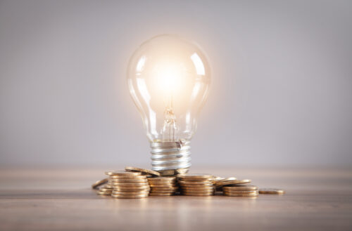 Light bulb and stack of coins on the desk. Saving energy and money